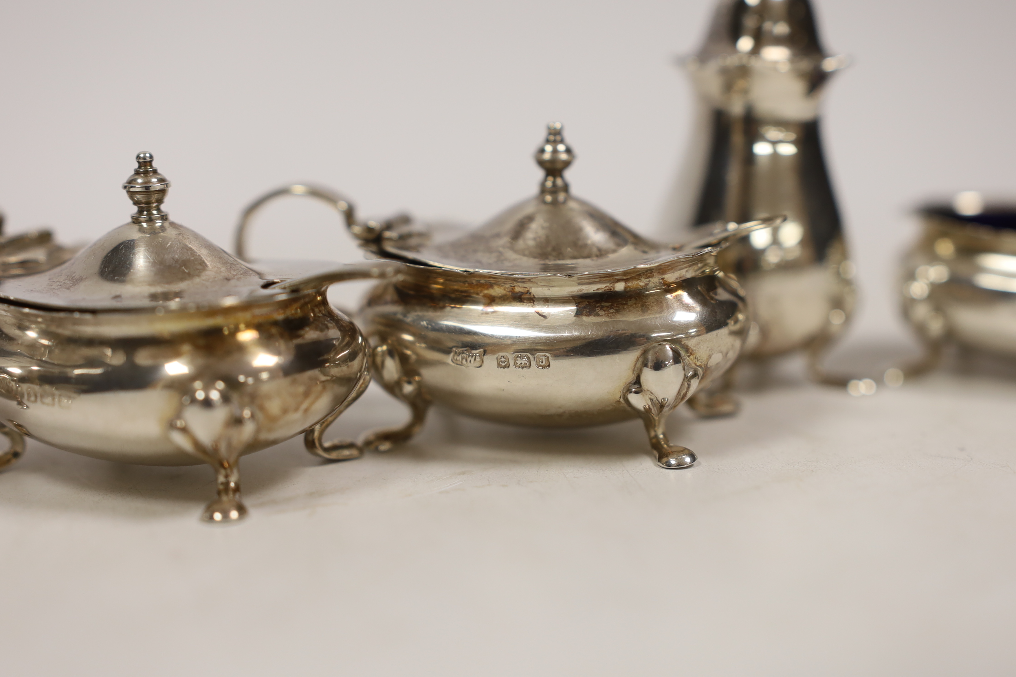 A George V silver three piece condiment set, Adie Brothers, Birmingham, 1928 and two matching spoons, together with a matched three piece silver condiment set and two silver spoons.